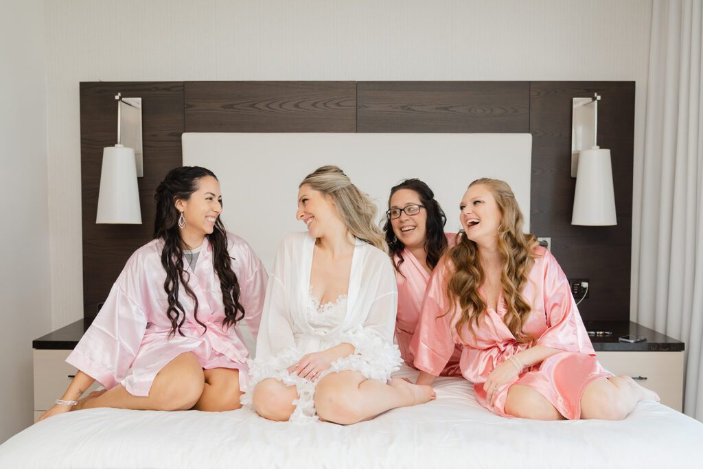 Bride and bridesmaids sitting on bed before ceremony