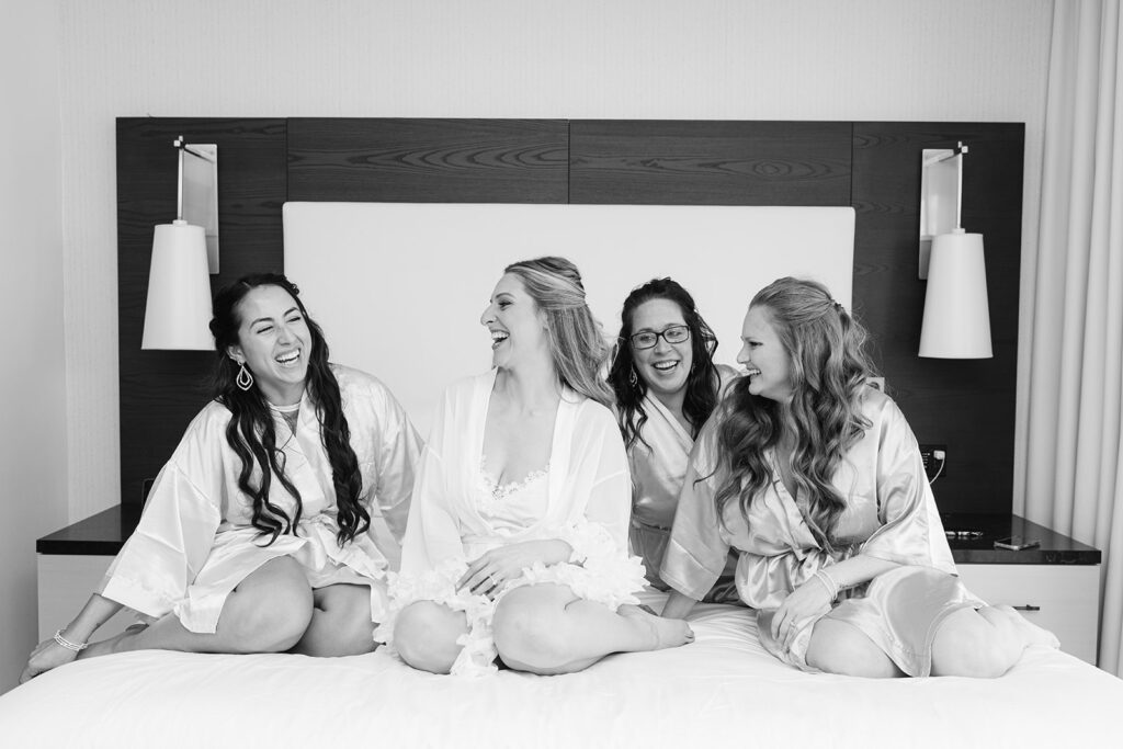 Bride and bridesmaids sitting on bed before ceremony
